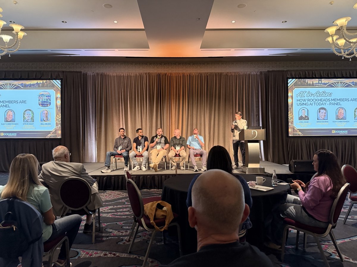 Five panelists seated on stage beneath screens showing an AI discussion.